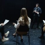 Group of actors in rehearsal with director, practicing for a theater performance.